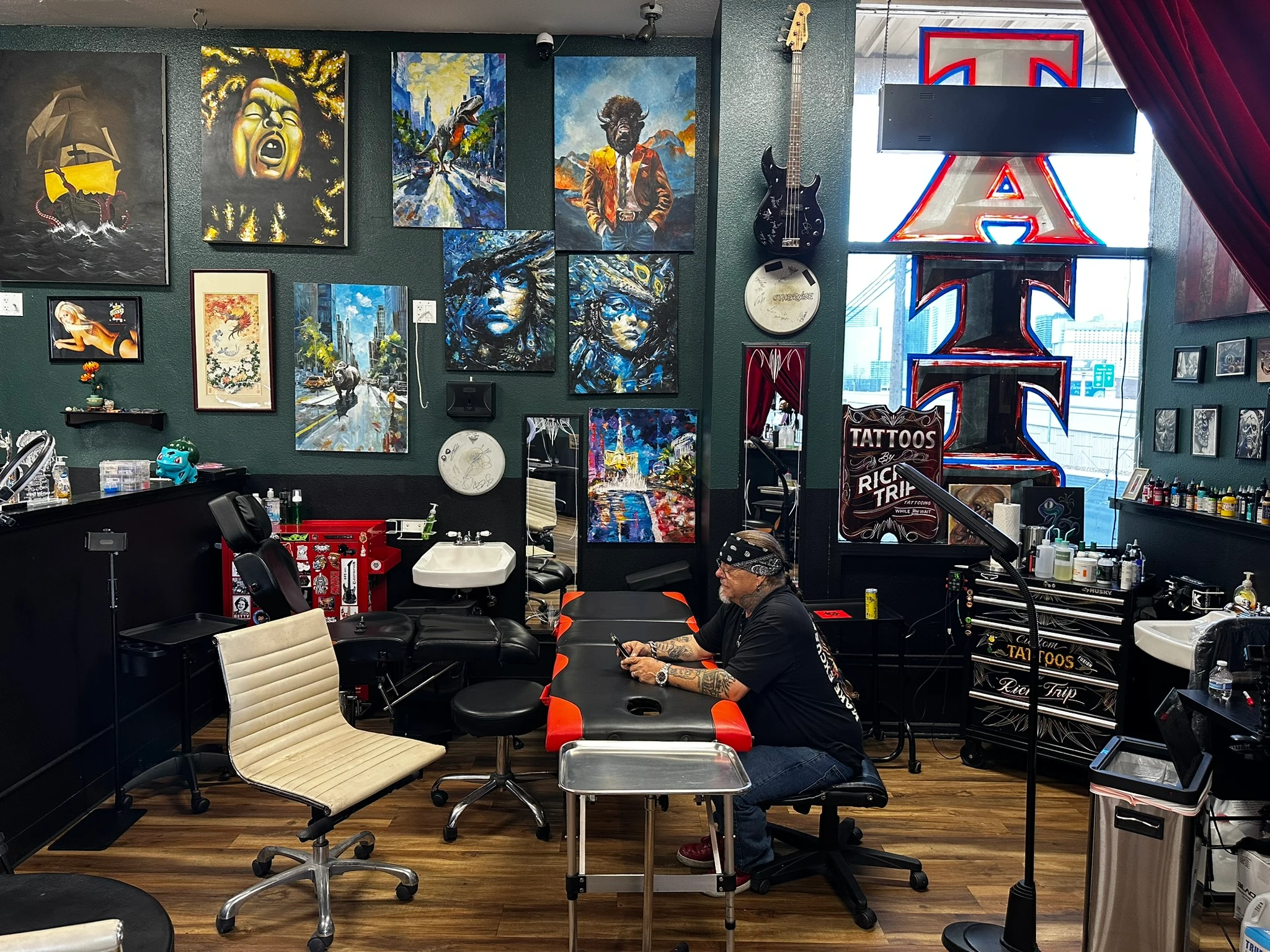 Wide view of Rick Trip's working tattoo studio, showing art-covered green walls, tattoo chairs and Rick seated at a workstation